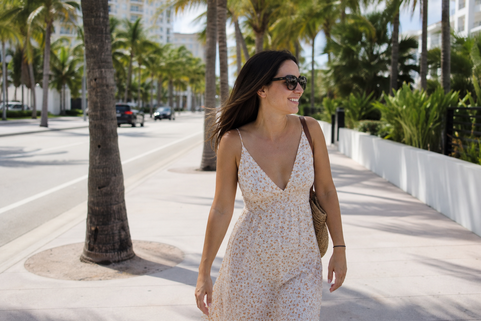 A smiling woman in a sundress strolling past boutique storefronts on a sunny South Florida afternoon
